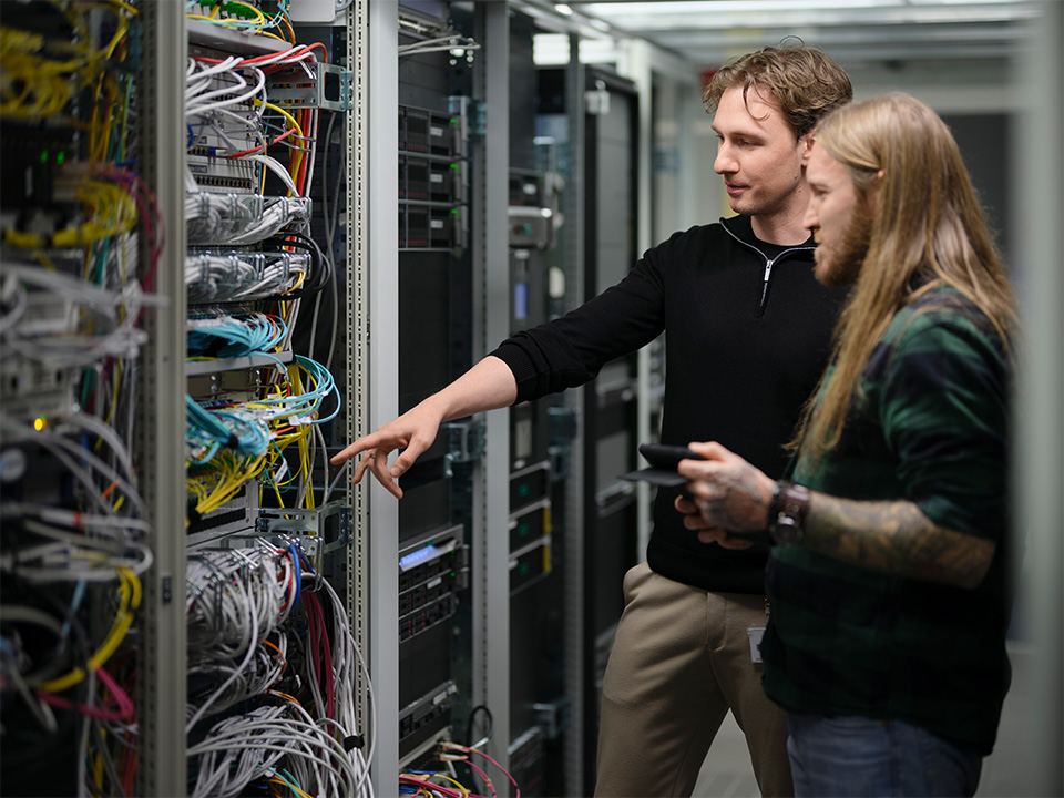 Zwei Mitarbeiter stehen vor einen Serverschrank.