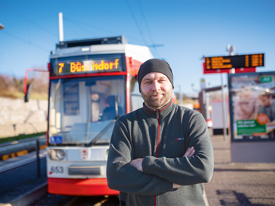 Straßenbahnfahrer steht mit verschränkten Armen vor seiner Bahn.